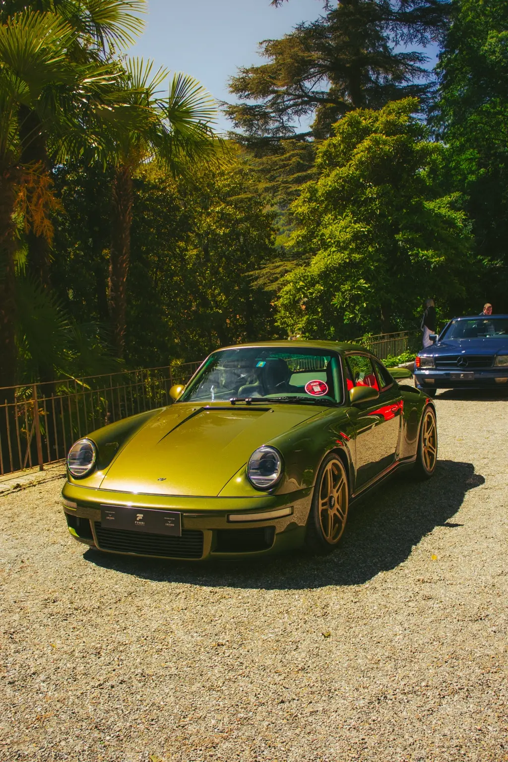 Porsche verde esposta tra gli alberi con il Lago di Como sullo sfondo