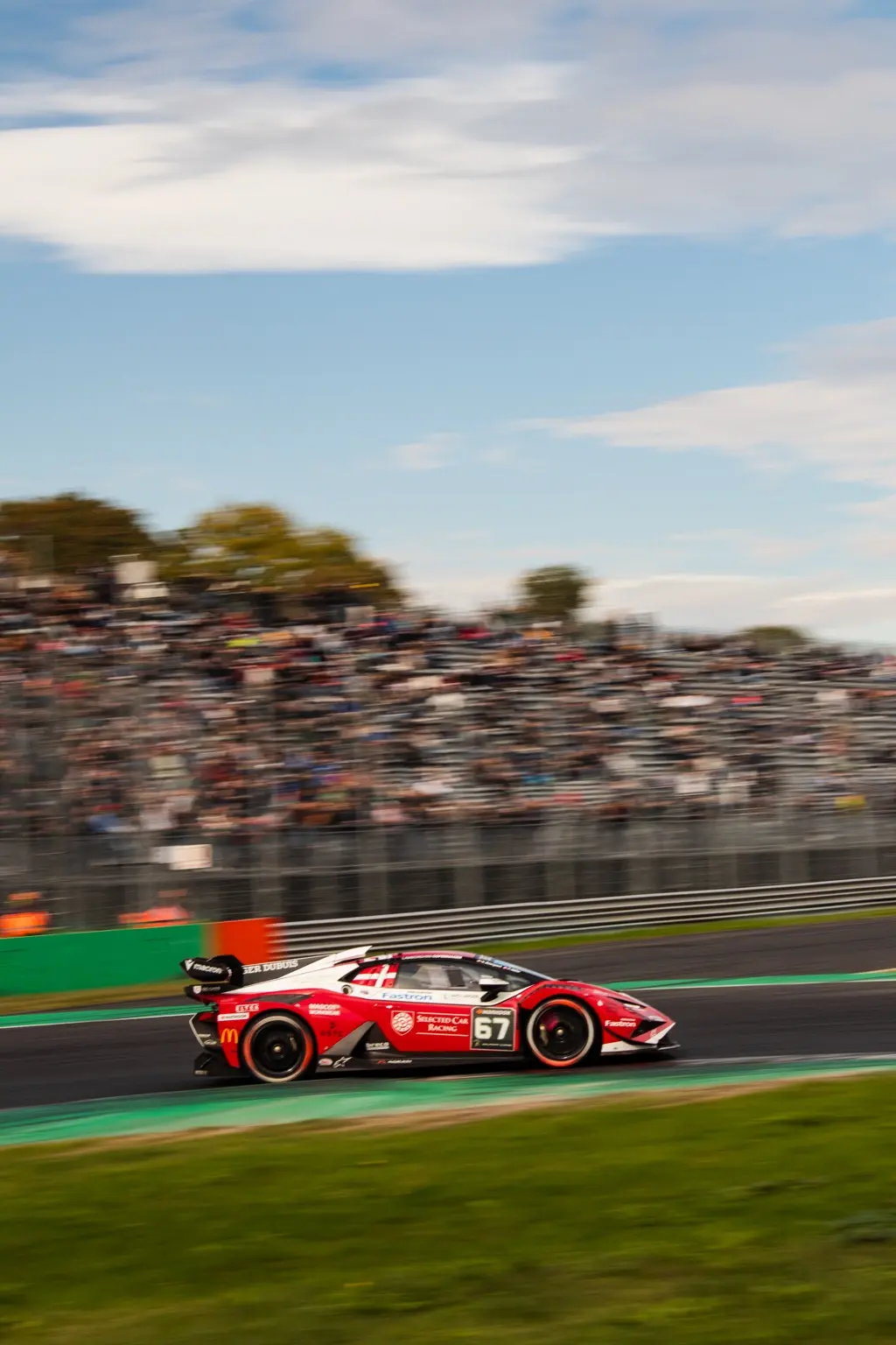 Red number 67 Lamborghini race car passing the Monza grandstand